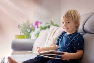 Tatlı sarışın çocuk, evde kitap okuyor, gülüyor, aile mutluluğu.