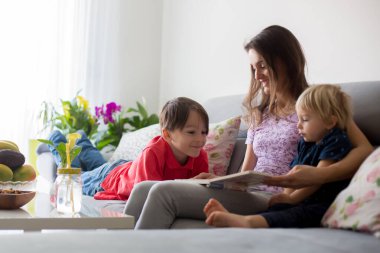 Genç bir kadın, üç çocuklu bir anne, evde kitap okuyor, sarılıyor ve gülüyor, aile mutluluğu.
