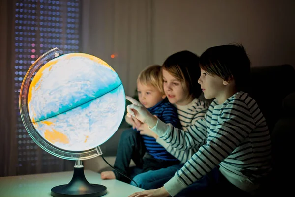 Little children, brothers, looking at illuminated globe, exploring the world, learning