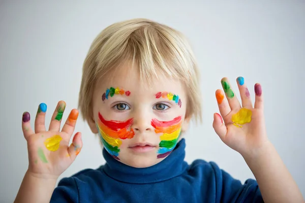 美しいですブロンド幼児男の子とともに虹彩塗装彼の顔と乱雑な手 幸せな笑顔 — ストック写真
