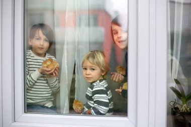 Aile, yavruları kucağında tutan çocuklar, pencerenin arkasında, evde, koronavirüs yüzünden karantinada.