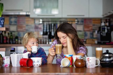 Genç anne, sabahları bebeğiyle çok kahve içiyor, mutfakta oturuyor.