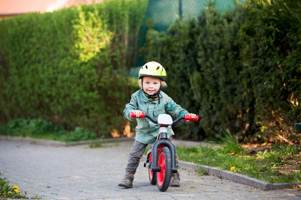 ブロンドの小さな幼児自転車に乗ってヘルメットをかぶって晴れた日に遊び場で遊ぶ — ストック写真