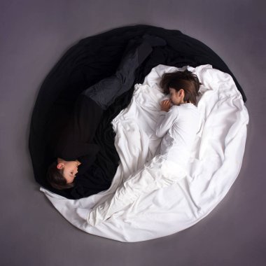 İki çocuk, siyah-beyaz giyinmiş, Yin-Yang çemberinde yerde yatıyor, izole bir görüntü.
