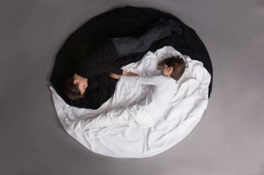 İki çocuk, siyah-beyaz giyinmiş, Yin-Yang çemberinde yerde yatıyor, izole bir görüntü.