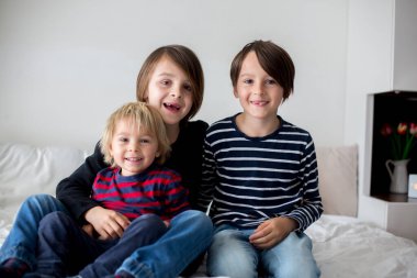 Üç çocuk, erkek kardeşler, yatakta gülüyorlar, kıkırdıyorlar ve gıdıklıyorlar.