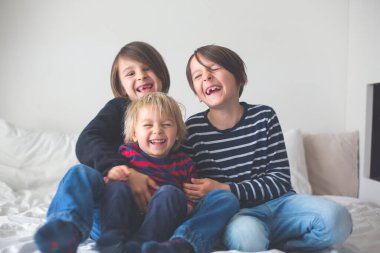 Üç çocuk, erkek kardeşler, yatakta gülüyorlar, kıkırdıyorlar ve gıdıklıyorlar.