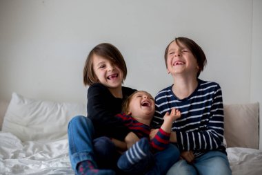 Üç çocuk, erkek kardeşler, yatakta gülüyorlar, kıkırdıyorlar ve gıdıklıyorlar.