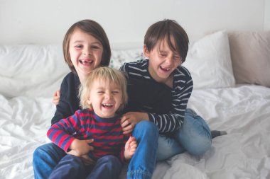 Üç çocuk, erkek kardeşler, yatakta gülüyorlar, kıkırdıyorlar ve gıdıklıyorlar.