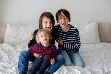 Üç çocuk, erkek kardeşler, yatakta gülüyorlar, kıkırdıyorlar ve gıdıklıyorlar.