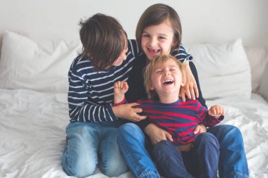 Üç çocuk, erkek kardeşler, yatakta gülüyorlar, kıkırdıyorlar ve gıdıklıyorlar.