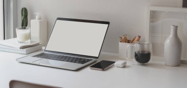 Boş dizüstü bilgisayarı ve beyaz ahşap masadaki ofis malzemeleriyle minimum çalışma alanı.