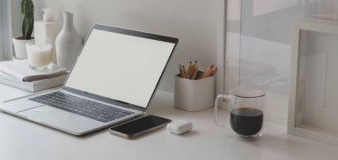 Boş dizüstü bilgisayarı ve beyaz ahşap masadaki ofis malzemeleriyle minimum çalışma alanı.