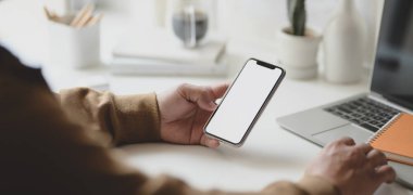 Modern iş yerinde boş ekran akıllı telefonu tutan serbest çalışan genç bir erkeğin görüntüsü. 