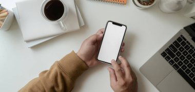 Genç serbest çalışan bir erkeğin modern işyerinde boş ekranlı akıllı telefonu tutması. 
