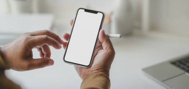 Modern işyerindeki boş ekran akıllı telefonuna bakan serbest çalışan genç bir erkeğin görüntüsü. 