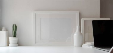 Beyaz ahşap masa ve beyaz duvar arkaplanı üzerindeki çerçeve ve dekorasyonlarla en az ofis odası