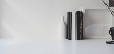Beyaz ahşap masa ve beyaz duvar arkaplanı üzerine kitap ve ofis malzemeleri olan modern ofis odası. 
