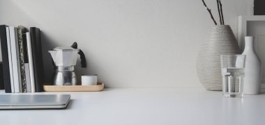 Beyaz ahşap masa ve beyaz duvar arkaplanı üzerinde kopya alanı, kitap ve ofis malzemesi bulunan en az çalışma alanı 