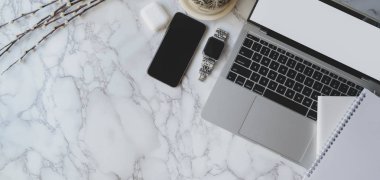 Laptop bilgisayarı, akıllı telefon ve ofis malzemeleriyle mermer masa arkasında şık bir çalışma alanı. 