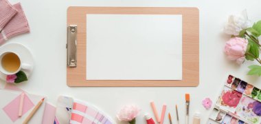Pembe kadın ressamın çalışma alanının, eskiz kağıdı ve beyaz masa arkaplanındaki boya araçlarıyla genel görüntüsü. 