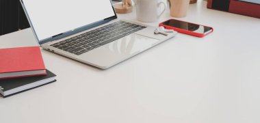 Dizüstü bilgisayar ve ofis malzemeleriyle pencerelerin yanındaki beyaz masada rahat çalışma alanının görüntüsü.