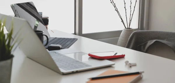 Schnappschuss vom komfortablen Arbeitsplatz mit Laptop und Bürobedarf auf weißem Tisch neben den Fenstern — Stockfoto
