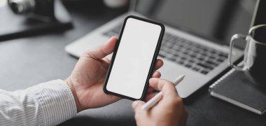 Profesyonel iş adamının karanlık modern ofis odasında boş ekran akıllı telefonu tutarken çekilmiş görüntüsü.