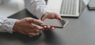 İş adamının karanlık, modern çalışma alanındaki akıllı telefonuyla bilgi arayışına yakından bakın.