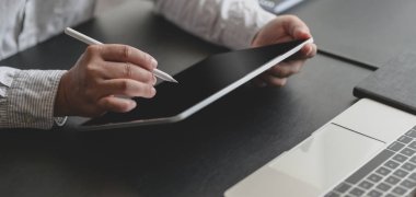 Modern ofis odasında tabletle başarılı bir iş adamının projesi üzerinde çalışırken çekilmiş görüntüsü. 