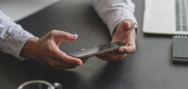 İş adamının karanlık, modern çalışma alanındaki akıllı telefonuyla bilgi arayışına yakından bakın.