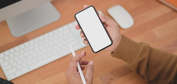 Beskuren bild av man som håller blank skärm smartphone medan du arbetar med sitt projekt på sin mysiga arbetsplats — Stockfoto