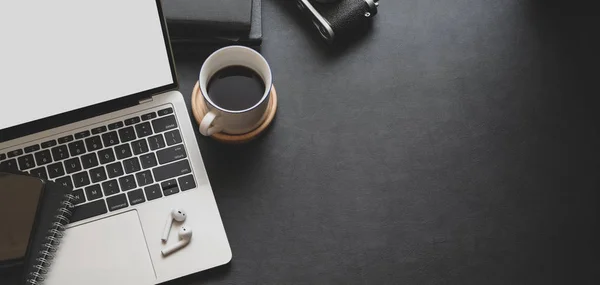 Vista de cerca del espacio de trabajo de moda oscura con computadora portátil, taza de café y suministros de oficina con espacio para copias —  Fotos de Stock