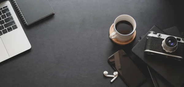 Vista de cerca del espacio de trabajo de moda oscura con computadora portátil, taza de café y suministros de oficina con espacio para copias — Foto de Stock