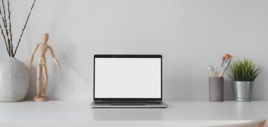 Boş ekran dizüstü bilgisayarı beyaz masa ve beyaz duvar arkaplanı süslemeleri olan minimal iş yerinde aç 