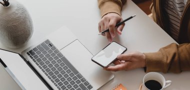 Projesi üzerinde çalışan serbest çalışan erkek çalışanın rahat offie odasında boş ekran akıllı telefonuyla yakın plan görüntüsü 
