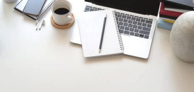 Dizüstü bilgisayar ve ofis malzemeleriyle beyaz ahşap masada rahat çalışma alanının görüntüsü. 