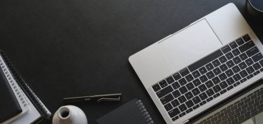 Laptop bilgisayarı ve ofis malzemeleriyle siyah masa arkaplanda fotokopi alanı olan modaya uygun ofis odası görüntüsü. 