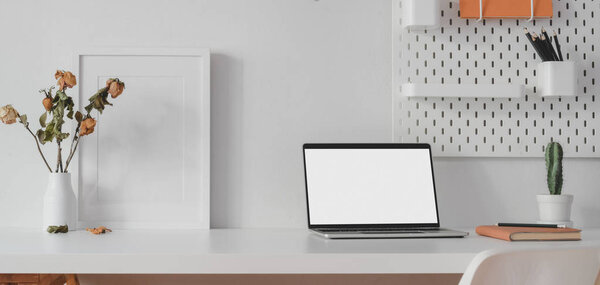 Modern workspace with open blank screen laptop computer and mock up frame with decorations on white wooden table 