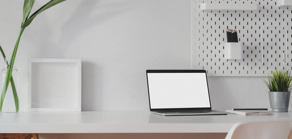 Минимальное рабочее место с открытым пустым экраном ноутбука и макет рамку с украшениями на белом деревянном столе
 