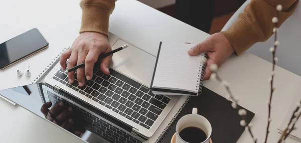 Tiro recortado de freelancer masculino trabalhando em seu projeto ao coletar ideias de notebook em espaço de trabalho confortável — Fotografia de Stock