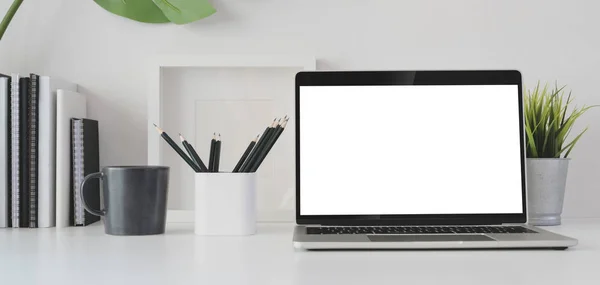 Обрезанный снимок современной офисной комнаты с чистым экраном ноутбука и офисных принадлежностей на белом столе — стоковое фото