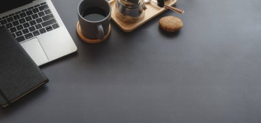 Karanlık masa arkasında dizüstü bilgisayarı ve ofis malzemeleri olan karanlık ve modern iş yeri manzarası