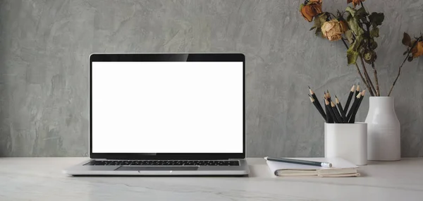 Przycięte ujęcie z otwartym pustym ekranie laptopa z wyposażeniem biurowym i dekoracjami wazonu suchych róż — Zdjęcie stockowe