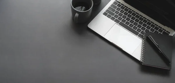 Overhead shot van donkere stijlvolle werkruimte met laptop computer zwart notebook op zwarte tafel achtergrond — Stockfoto