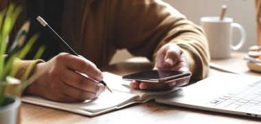 Yakın plan genç adam rahat ofis odasında akıllı telefonuyla projesinde çalışıyor. 