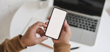 Projeyi rahat bir iş yerinde çalışırken elinde boş ekran akıllı telefonu tutan adamın üst görünümü 