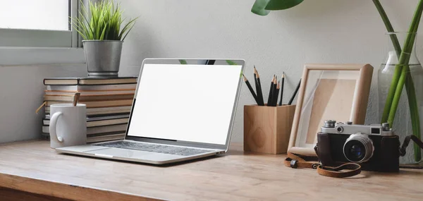 Captura recortada de espacio de trabajo cómodo con computadora portátil de pantalla en blanco, suministros de oficina y cámara en la mesa de madera —  Fotos de Stock