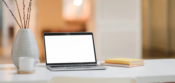 Colpo ritagliato di comodo posto di lavoro con computer portatile mock up, tazza di caffè e forniture per ufficio con sfondo ufficio — Foto Stock