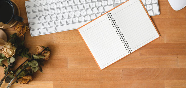 Top view of comfortable workplace with notebook and keyboard computer on wooden table with dry roses decorations 